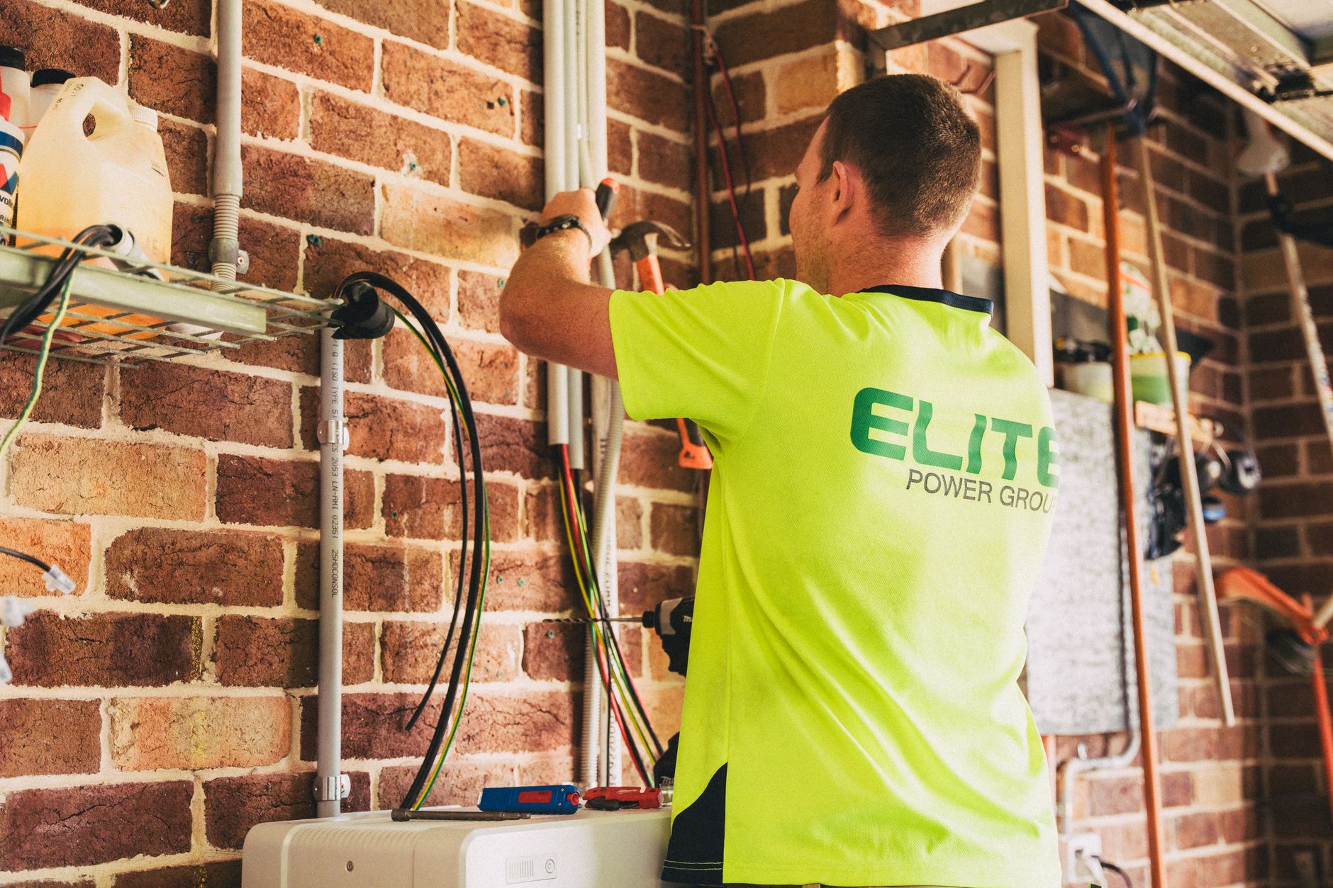 White wall mounted home battery above a gray inverter in a garage