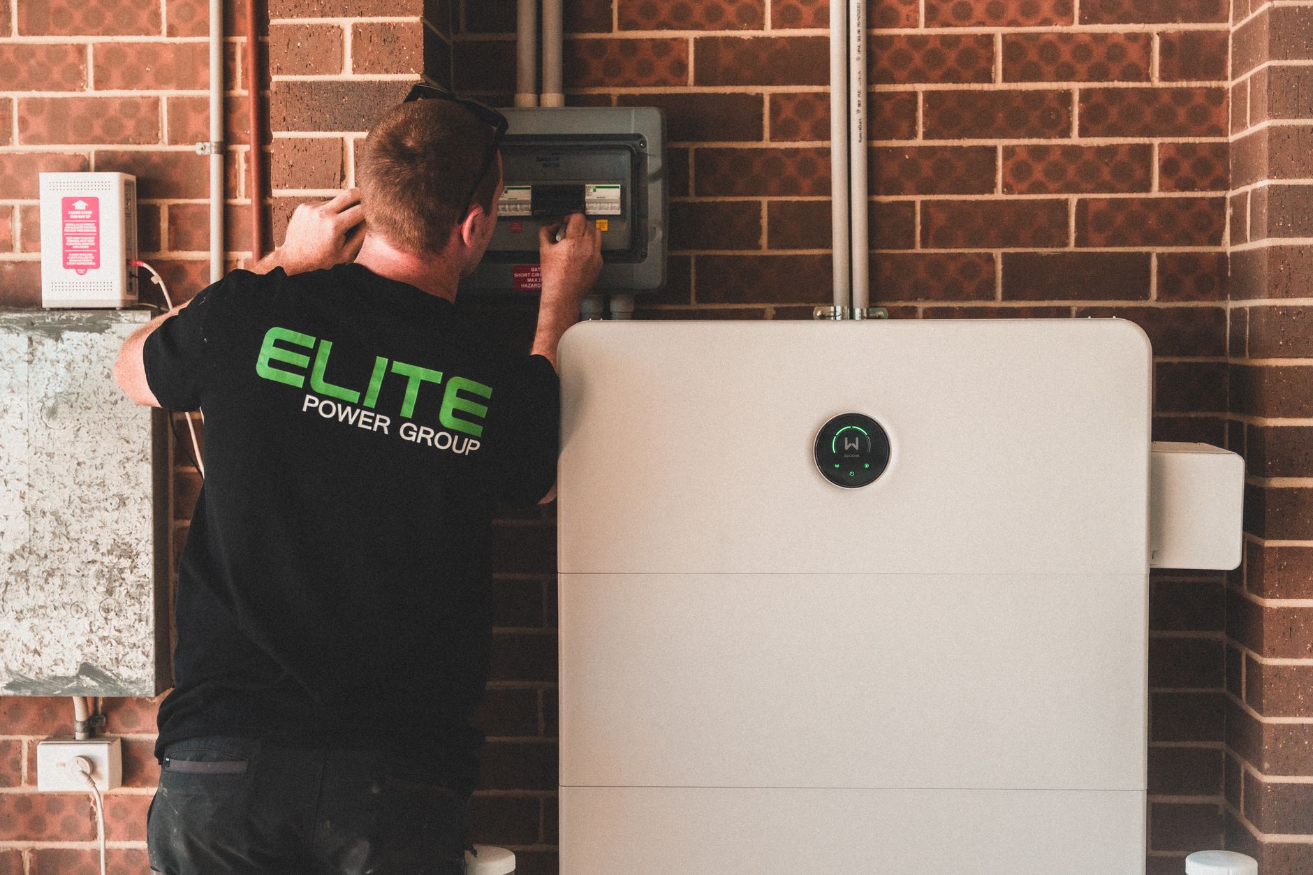 an electrician mounting a white home battery on a garage wall