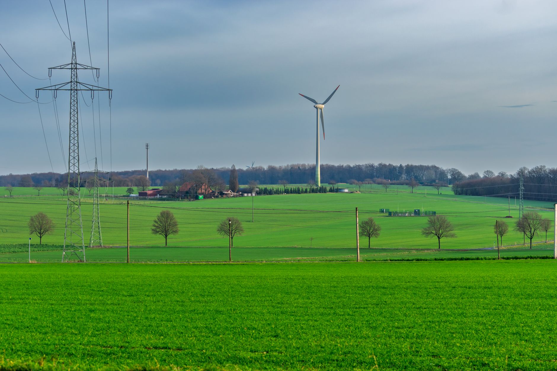 Tall steel lattice tower holding a three-blade wind turbine above green farmland